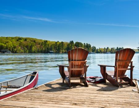 Two wooden chairs on a pier next to a boat overlooking Grand Lake.