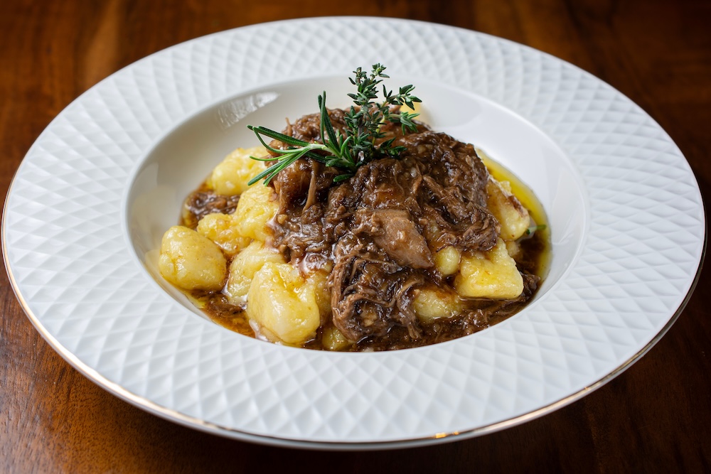 Short rib ragout in ceramic white bowl over wooden table